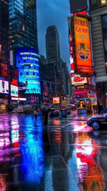 Neon lights and colorful reflections illuminate the wet streets of Broadway at night