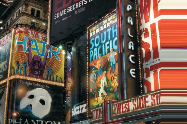 Broadway signs feature iconic musical posters like Hair and South Pacific displayed at night