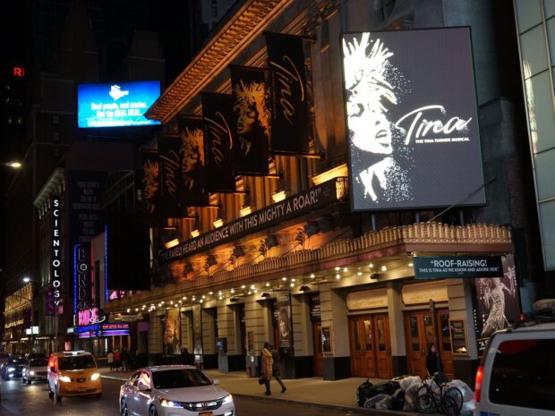 Broadway theater signs and banners featuring Tina the musical on a busy street at night