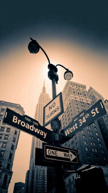 Street signs on Broadway and West 34th st in a cityscape with tall buildings and a sunset sky