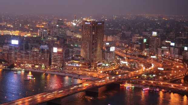 Night view of Cairo city skyline with illuminated buildings and busy river bridge