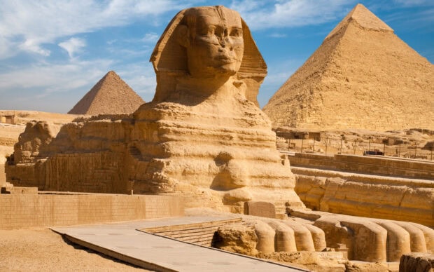 The Great Sphinx of Cairo Egypt with the pyramids in the background under a blue sky