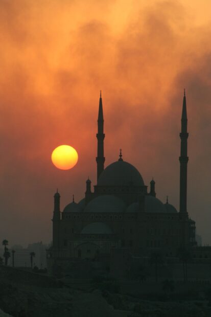 Silhouette of historic Cairo mosque at sunset with glowing sun in Egypt sky