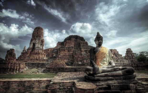 Ancient temple ruins with a seated Buddha statue in Cambodia under a cloudy sky