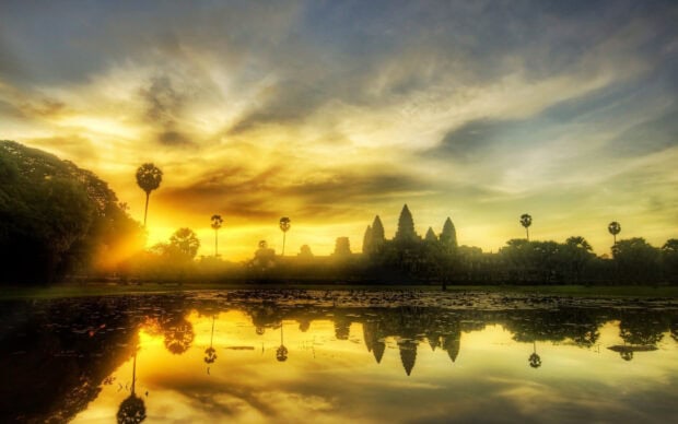 Ancient temples in Cambodia reflected in a peaceful lake during sunrise with dramatic sky