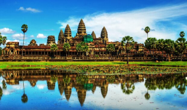 Ancient Cambodia temple with palm trees reflected in water under blue sky