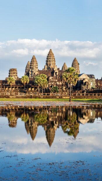 Ancient Cambodia temple reflected in a tranquil water body surrounded by palm trees