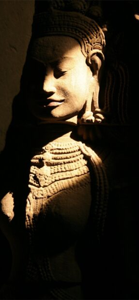 A detailed carving of an ancient Cambodia statue illuminated by soft light on a dark background