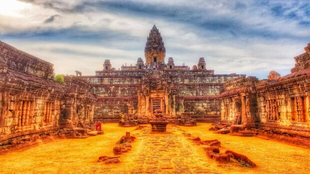Ancient Cambodian temple with stone carvings and visitors under cloudy sky