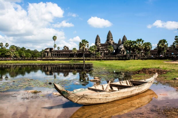 Ancient Cambodia temple with a wooden boat by the water under a blue sky