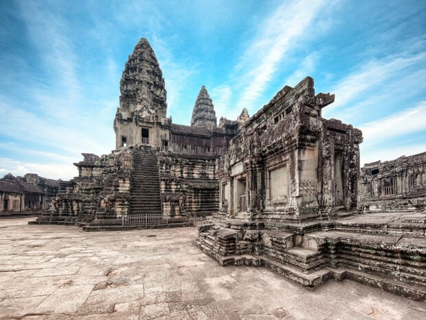 Ancient Cambodia temple ruins under a bright blue sky with detailed stone carvings