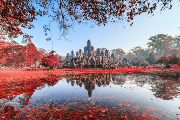 Ancient temple ruins in Cambodia surrounded by red foliage and reflected in water
