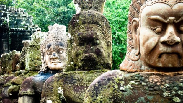 Ancient Cambodia statues covered with moss standing in a row at a historic temple site