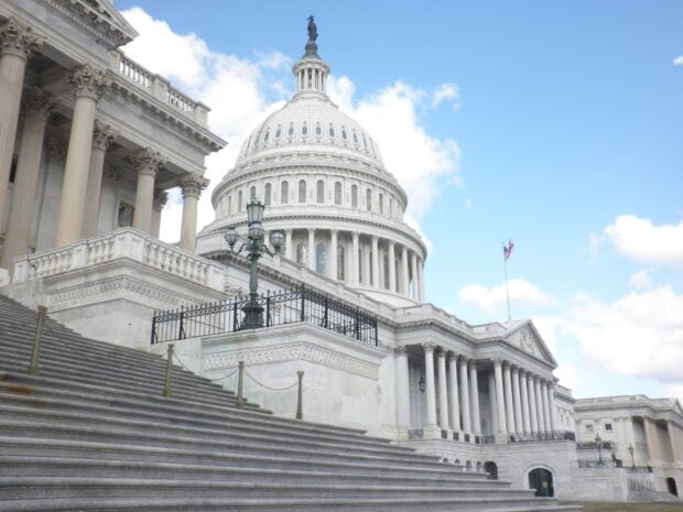 The Capitol Hill building with white columns and stairs under a blue sky