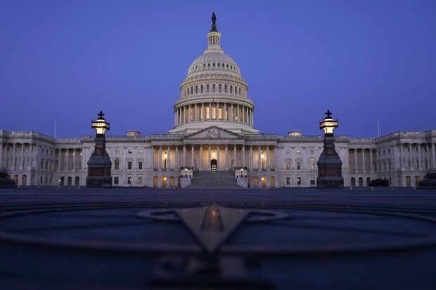 The Capitol Hill building illuminated at dusk with a clear blue sky in the background