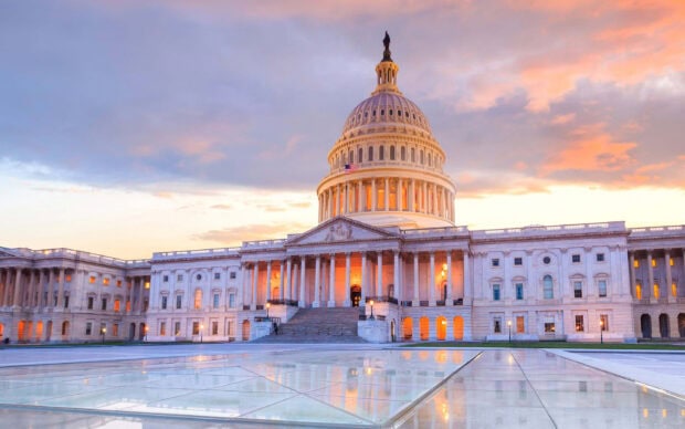 Capitol Hill at sunset with illuminated windows and a reflective plaza in front