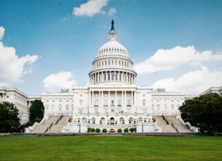 The Capitol Hill building stands majestically under a bright blue sky with lush green grass in front