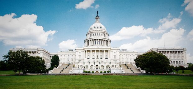 The Capitol Hill building stands majestically under a bright blue sky with lush green grass in front