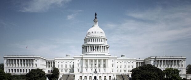 The Capitol Hill building stands tall under a clear sky with lush green trees surrounding the structure