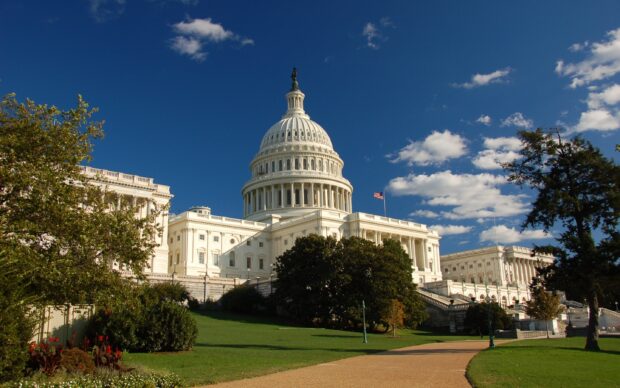 The Capitol Hill building surrounded by green trees and blue sky in clear weather