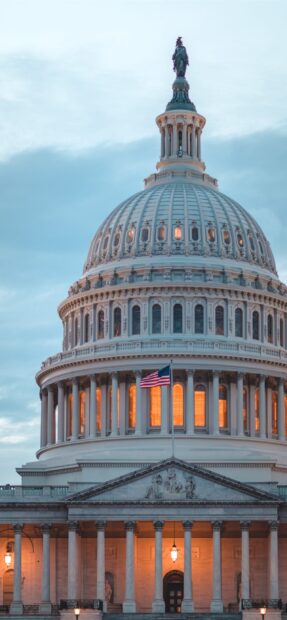 The Capitol Hill dome illuminated during twilight with the American flag flying in front