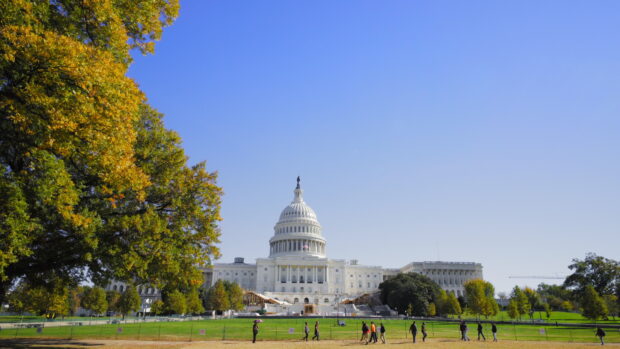 The Capitol Hill building with people walking on the grassy area under a clear blue sky