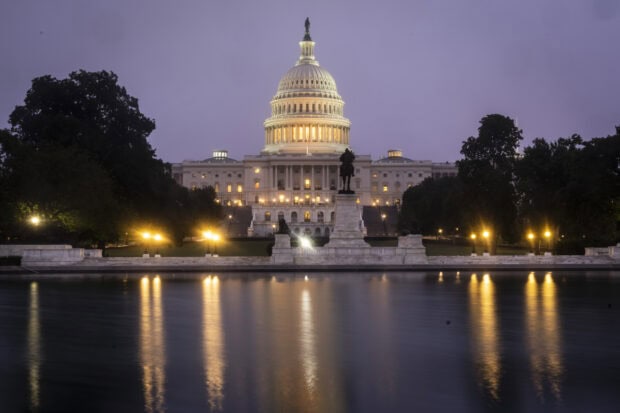 Capitol Hill at dusk with illuminated dome and statue reflecting on water