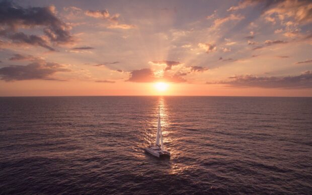 A catamaran sailing on the ocean during a beautiful sunset with dramatic clouds