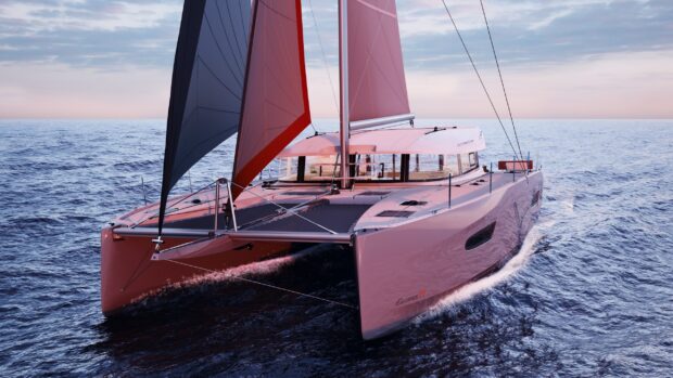 A sleek catamaran sailing on calm ocean waters during sunset with vibrant pink sails
