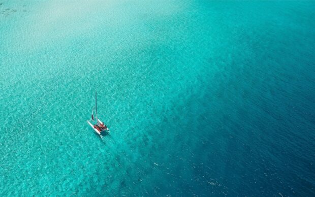 A catamaran sailing on clear turquoise water in a tranquil ocean scene