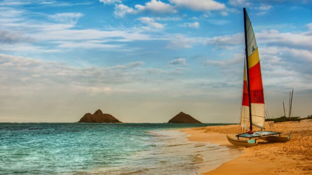 A catamaran on the sandy beach near turquoise ocean and distant islands under a cloudy sky