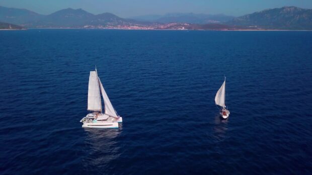 A catamaran sailing on calm deep blue sea near the coastline and distant mountains