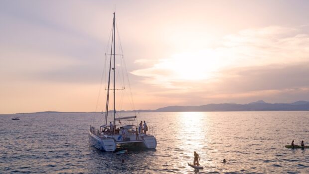 Catamaran sailing on the sea with people enjoying water activities at sunset
