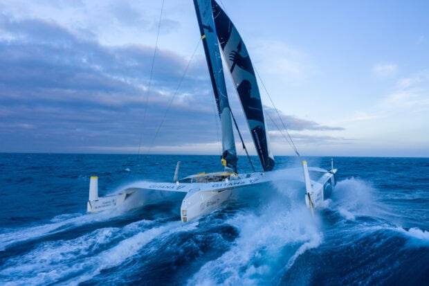 A catamaran sailing fast on the open sea with waves splashing around its hulls