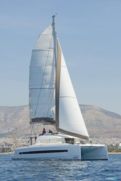 White catamaran sailing near the coast with mountains in the background