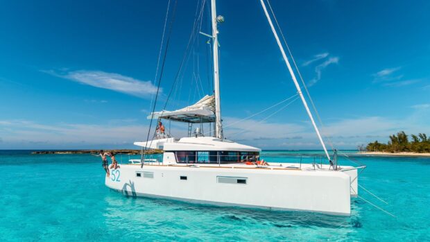 White catamaran sailing on clear turquoise ocean with people enjoying summer fun