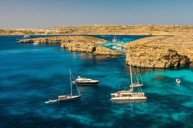 A catamaran sailing near rocky cliffs in clear blue water on a sunny day