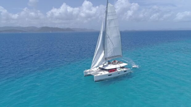 A catamaran sailing on clear blue ocean water near distant islands with a partly cloudy sky