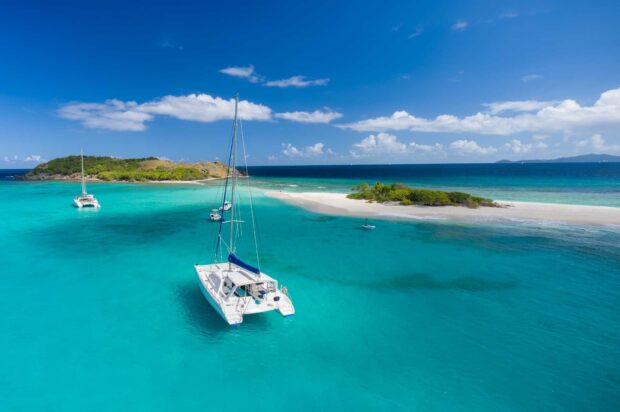 A catamaran sailing on clear turquoise waters near a tropical island under a bright blue sky