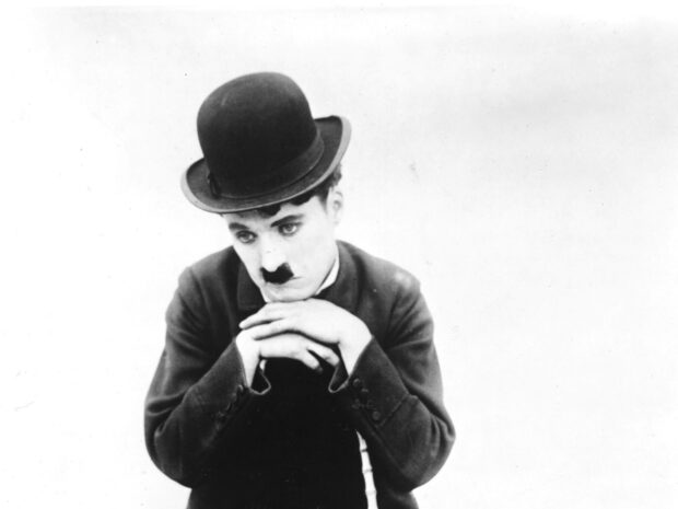 Charlie Chaplin wearing a bowler hat and resting his chin on his hands in a thoughtful pose