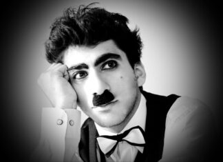 A man dressed as Charlie Chaplin with a mustache and bow tie resting his head on his hand