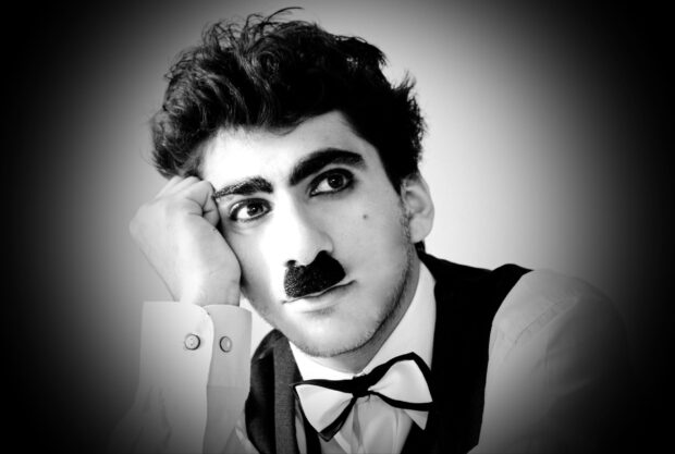 A man dressed as Charlie Chaplin with a mustache and bow tie resting his head on his hand