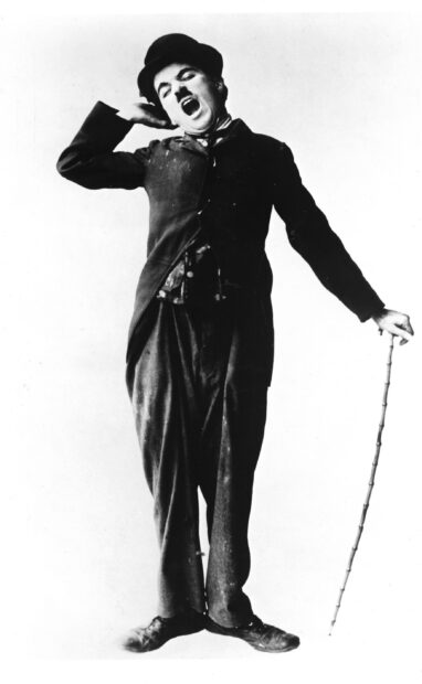 Charlie Chaplin is yawning and holding a cane in a classic pose