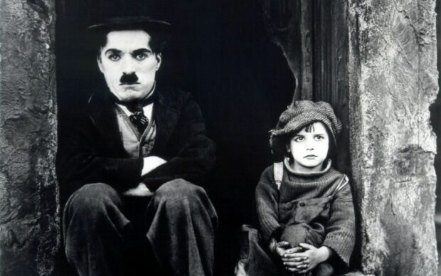 Charlie Chaplin sitting beside a young boy in a classic black and white scene