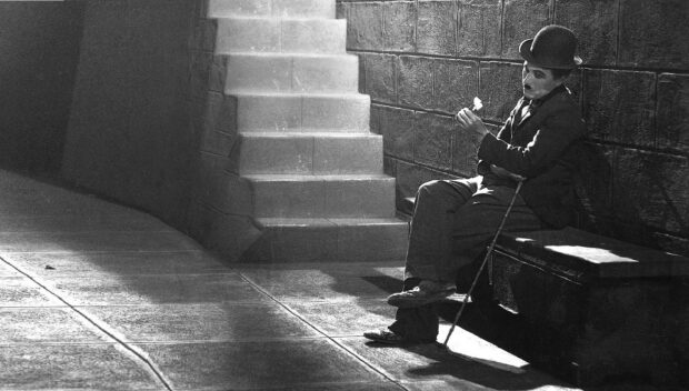 Charlie Chaplin sitting on a bench holding a flower in a black and white scene