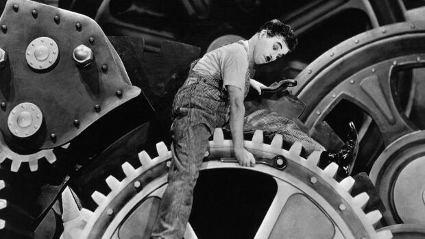 Charlie Chaplin working inside giant gears holding a wrench in a classic silent film scene