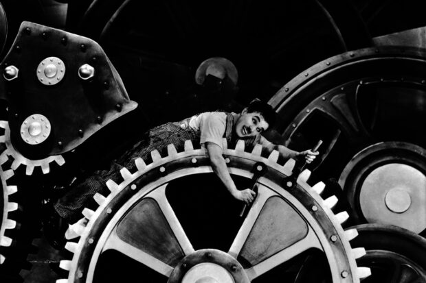 Charlie Chaplin working on large machinery gears in a classic black and white scene