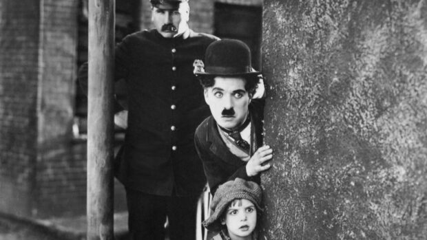 Charlie Chaplin character peeking from behind a wall with a child and a policeman in black and white