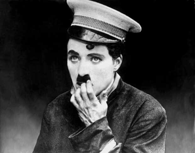 Charlie Chaplin character in costume with a hat and mustache covering his mouth with his hand