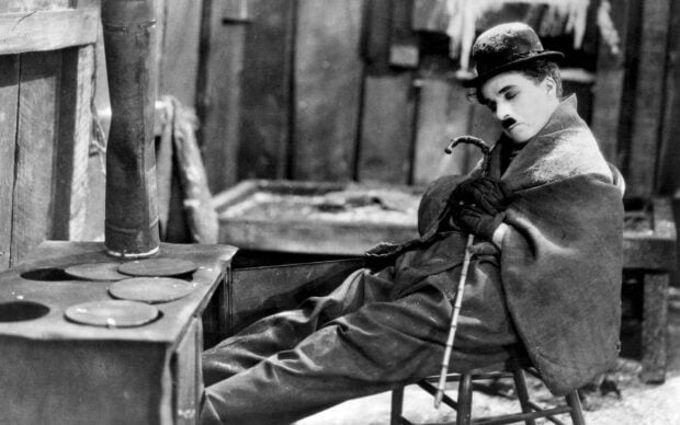 Charlie Chaplin resting on a chair wrapped in a blanket holding a cane